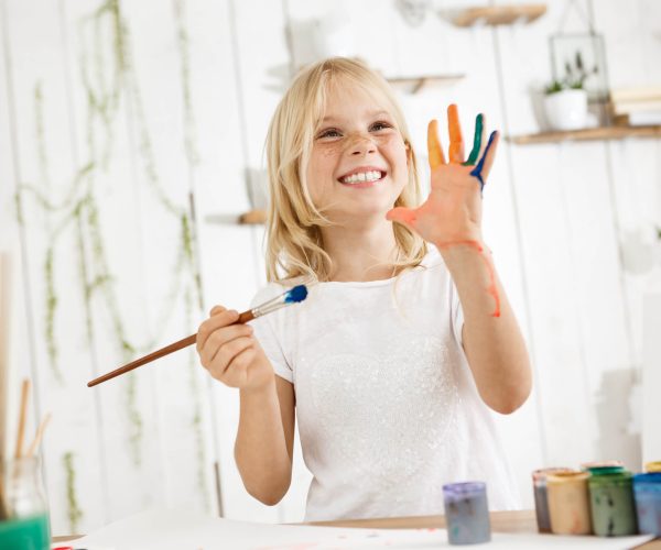 happy-playful-cute-freckled-blonde-girl-dressed-white-holding-brush-one-hand-showing-another-hand-which-she-messed-up-with-paint (1)